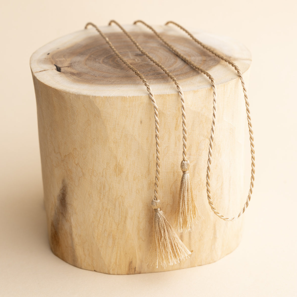 Béžová zapletaná šnúrka k rolničke na drevenom špalku